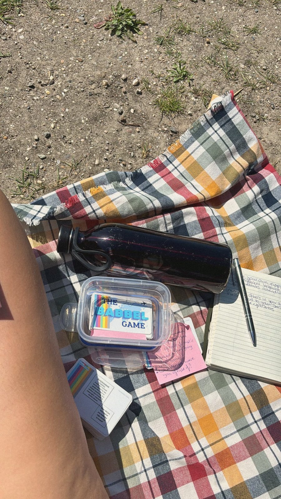 The Babbel Game box and cards on a checked picnic blanket next to a notebook